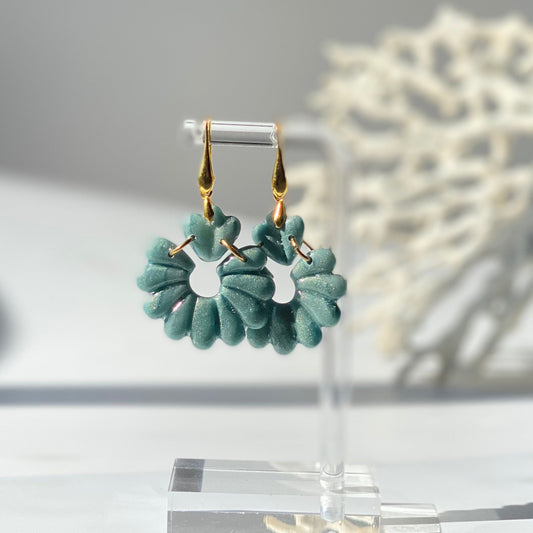 Boucles d’oreilles pendantes GAIA turquoise foncé métallisé en pâte polymère façonnée à la main, composées d’un cœur stylisé et d’une fleur ajourée aux pétales arrondis, avec attaches dorées – Nadd Concept.