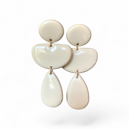 Variante Écrue du modèle LOUMA, boucles d’oreilles pendantes en pâte polymère faites main, au design graphique composé de trois formes arrondies